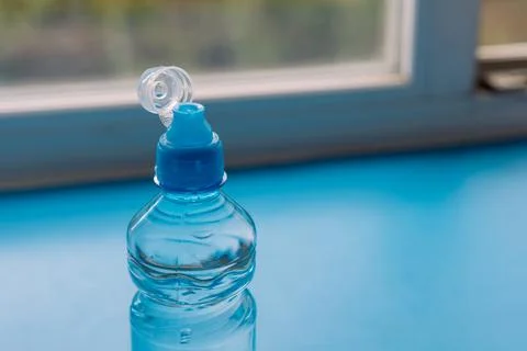 Open small plastic water bottle on blue windowsill near window Foto stock