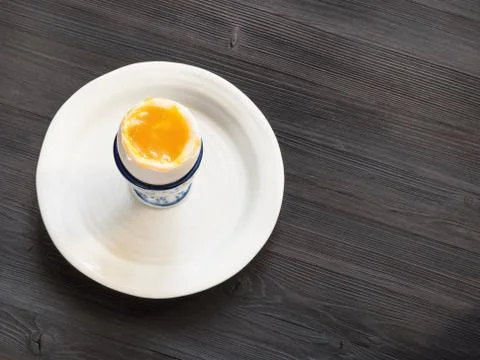 Open soft-boiled white egg in cup on plate on dark Stock Photos