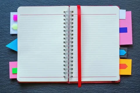 Open spiral bound notebook with bright colorful bookmarks on dark table. Stock Photos