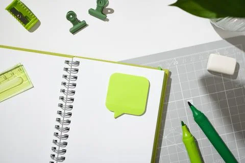 Open spiral notebook with a green speech bubble sticky note on a grey cutting Stock Photos