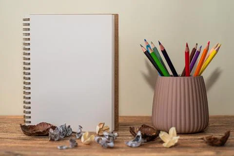 Open spiral notebook with white sheet, colored pencils in the glass next to i Stock Photos