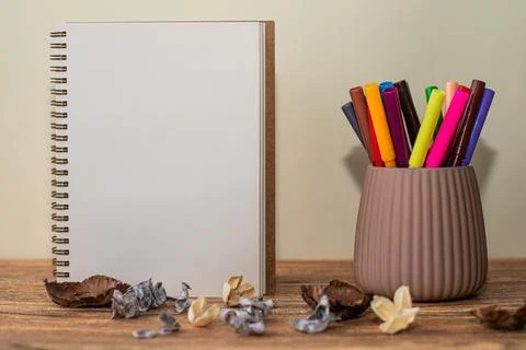 Open spiral notebook with white sheet, colored markers in the glass next to i Stock Photos