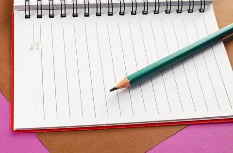 Open spring-loaded notebook and pencil on a pink and brown background. White  Stock Photos