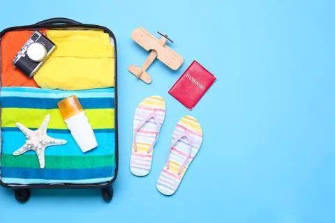 Open suitcase and beach objects on blue background, flat lay. Space for text 스톡 사진