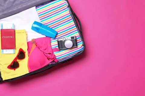 Open suitcase with beach objects on pink background, top view. Space for text 스톡 사진