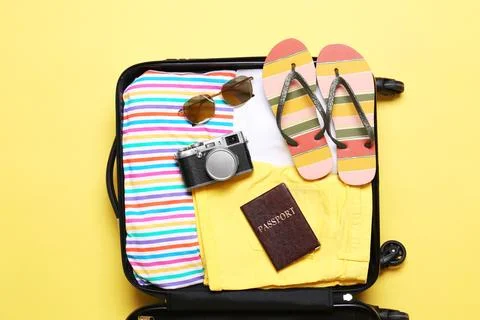 Open suitcase with beach objects on yellow background, top view Stock Photos