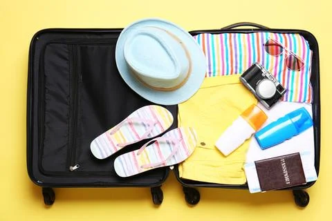 Open suitcase with beach objects on yellow background, top view Stock Photos