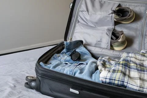 Open suitcase packed with clothes, shoes and sunglasses Stock Photos