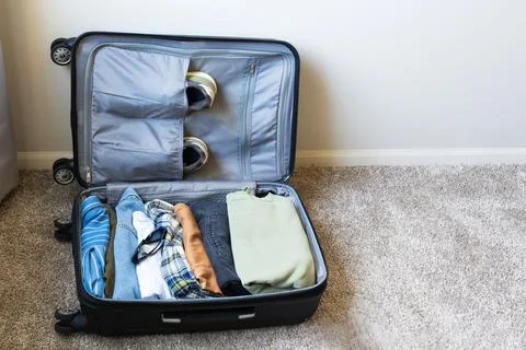 Open suitcase packed with clothes, shoes and sunglasses lying on the floor Stock Photos