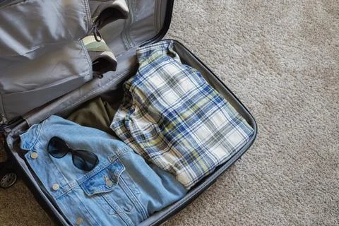 Open suitcase packed with clothes, shoes and sunglasses on the floor Stock Photos