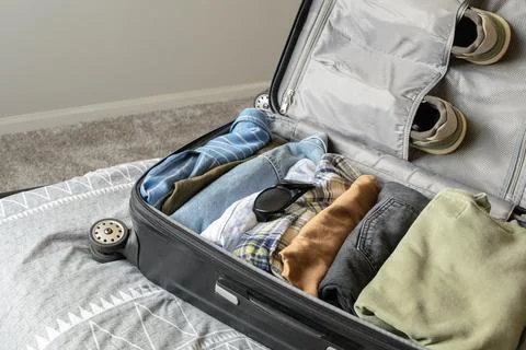 Open suitcase packed with folded clothes, shoes and sunglasses Stock Photos