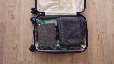 An open suitcase with things and a notebook lies on the wooden floor. Stock Photos