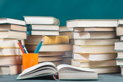 Open textbook on a desk against the background of stacks of books Stock Photos