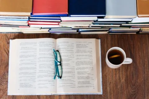 Open textbook, glasses, cup of tea and stack of old book on wooden table, edu Stock Photos