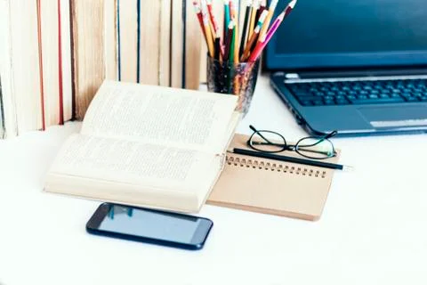 Open textbook, notebook, smartphone, laptop computer, stack of books educatio Stock Photos