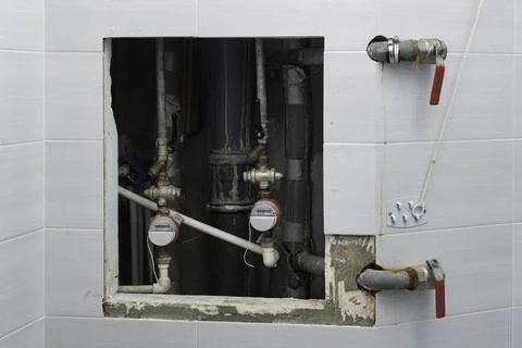 Open tiled wall access hatch reveals water meters, shutoff valves and corrode Stock Photos