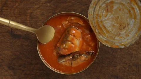 Open tin can of sprats in tomato sauce with a fork on wooden background Видео 337405809