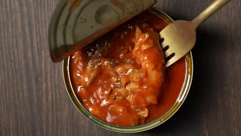 Open tin can of sprats in tomato sauce with a fork on wooden background 库存影片 338278339