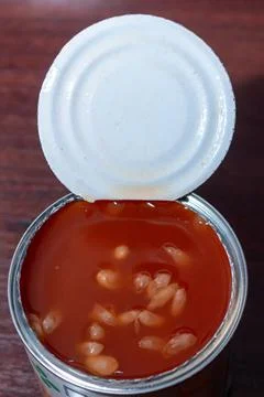 Open tin can with white beans in red tomato sauce on wooden table Фото