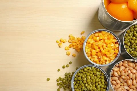 Open tin cans of conserved vegetables on wooden background, flat lay with spa Stock Photos