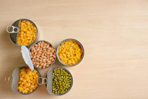 Open tin cans of conserved vegetables on wooden table, flat lay with space fo Foto stock