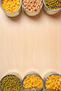 Open tin cans of conserved vegetables on wooden table, flat lay with space fo Foto stock