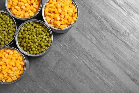 Open tin cans of conserved vegetables on grey table, flat lay with space for  Stock Photos