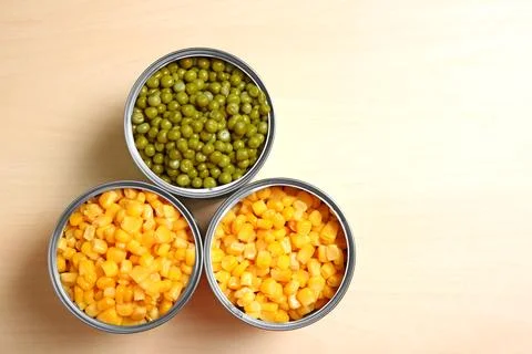 Open tin cans of conserved vegetables on wooden table, flat lay with space fo Foto stock