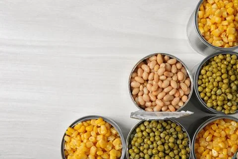 Open tin cans with different vegetables on light table, flat lay. Space for t Foto stock