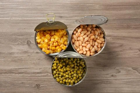 Open tin cans with different vegetables on wooden table, flat lay Foto stock