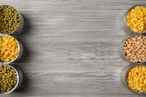 Open tin cans with different vegetables on wooden table, flat lay. Space for  Foto stock