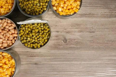Open tin cans with different vegetables on wooden table, flat lay. Space for  写真素材