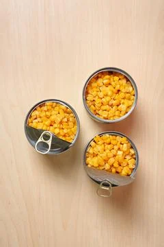 Open tin cans of sweet corn on wooden table, flat lay Foto stock