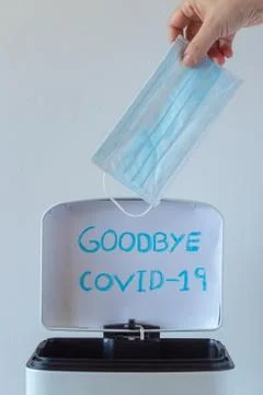 Open trash can with a goodbye message covid-19 and woman's hand pulling a mask Stock Photos
