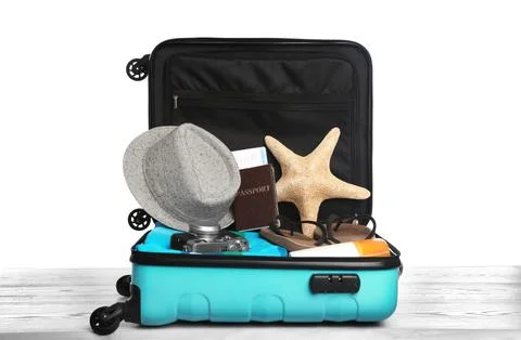 Open turquoise suitcase with different beach objects on wooden table, white b Stock Photos