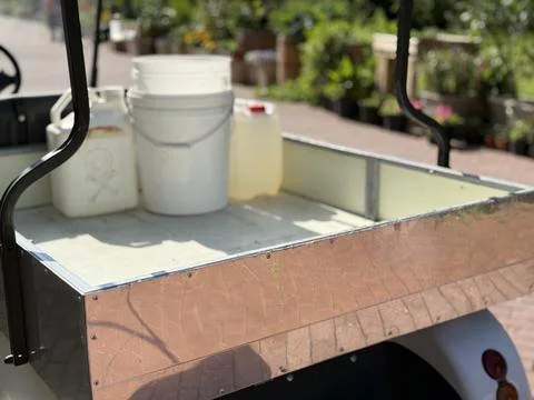 Open utility cart with empty white buckets and a jerry can on a sunny day Photos
