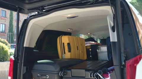 Open van trunk being unloaded with baggage on parking lot near, people putting Stock Footage 303749686