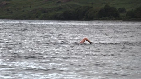 Open water swimmer doing front crawl in wide slow motion with green shoreline Stock-Footage 345107475