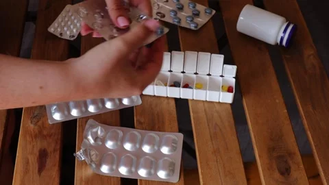 Open weekly pill organizer with multicolored capsules on wooden table surrounded Stock Footage 313794398