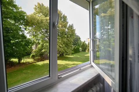 Open white PVC window overlooking a green residential garden with mature tree Fotos de archivo