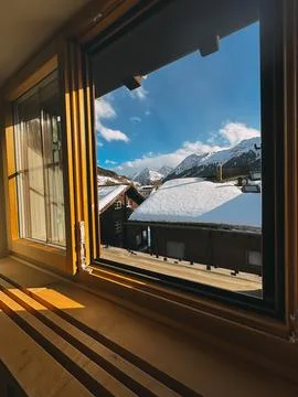 Open window overlooking snow covered roofs and majestic mountains in winter Stock Photos