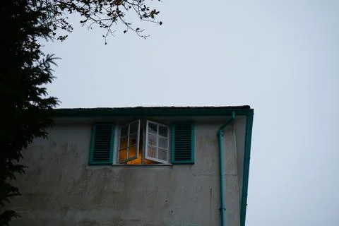 Open Window With Warm Light, Teal Shutters, And Tree Branches On Building In Stock Photos