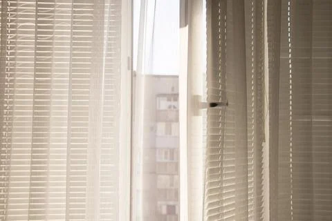 Open window with white blinds and curtains overlooking a neighboring house in Stock Photos