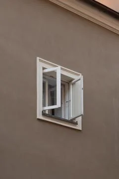 An open window with white frame on a solid brown stucco building facade Stock Photos
