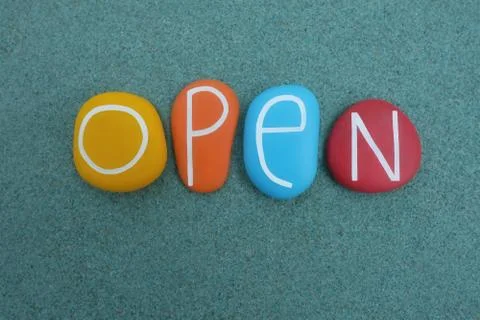 Open word composed with multicolored stone letters over green sand Stock Photos