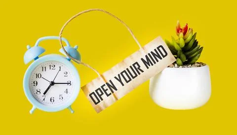 Open Your Mind written on a tag and a yellow background with a clock and a fl Stock Photos