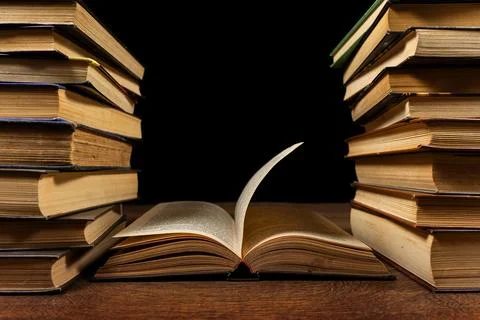 Opened book and stacks of old books on wooden desk in old library. Ancient bo Foto stock