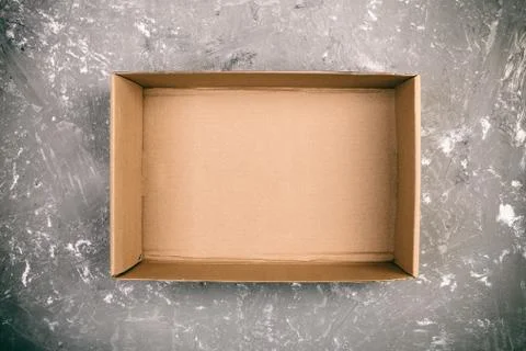 Opened brown blank cardboard box on cement gray background vintage, toned, to Stock Photos