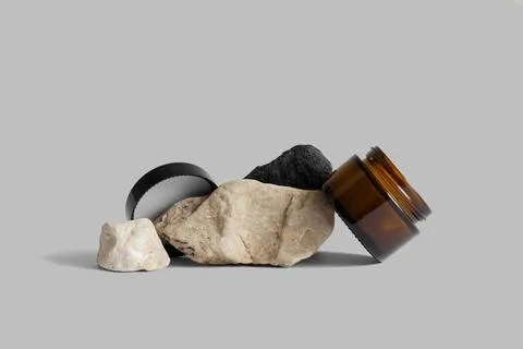 Opened brown glass jar with black cap on rocks, gray background, copy space. Stock Photos