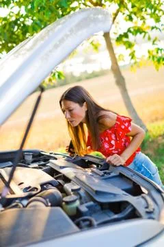Opened car hood and young woman looking for mistake on car engine, calling to Stock Photos